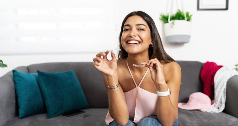 Person smiling while holding retainer in hand.